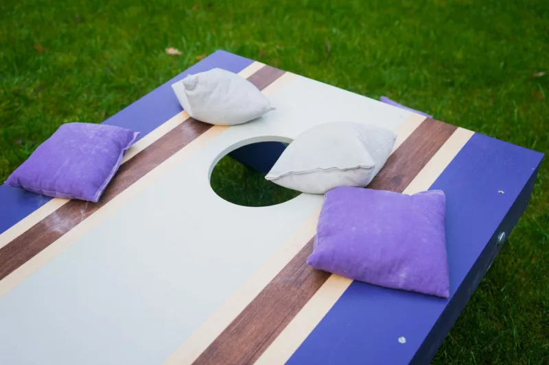 Blue, brown, and white striped cornhole board with four bean bags tossed on top