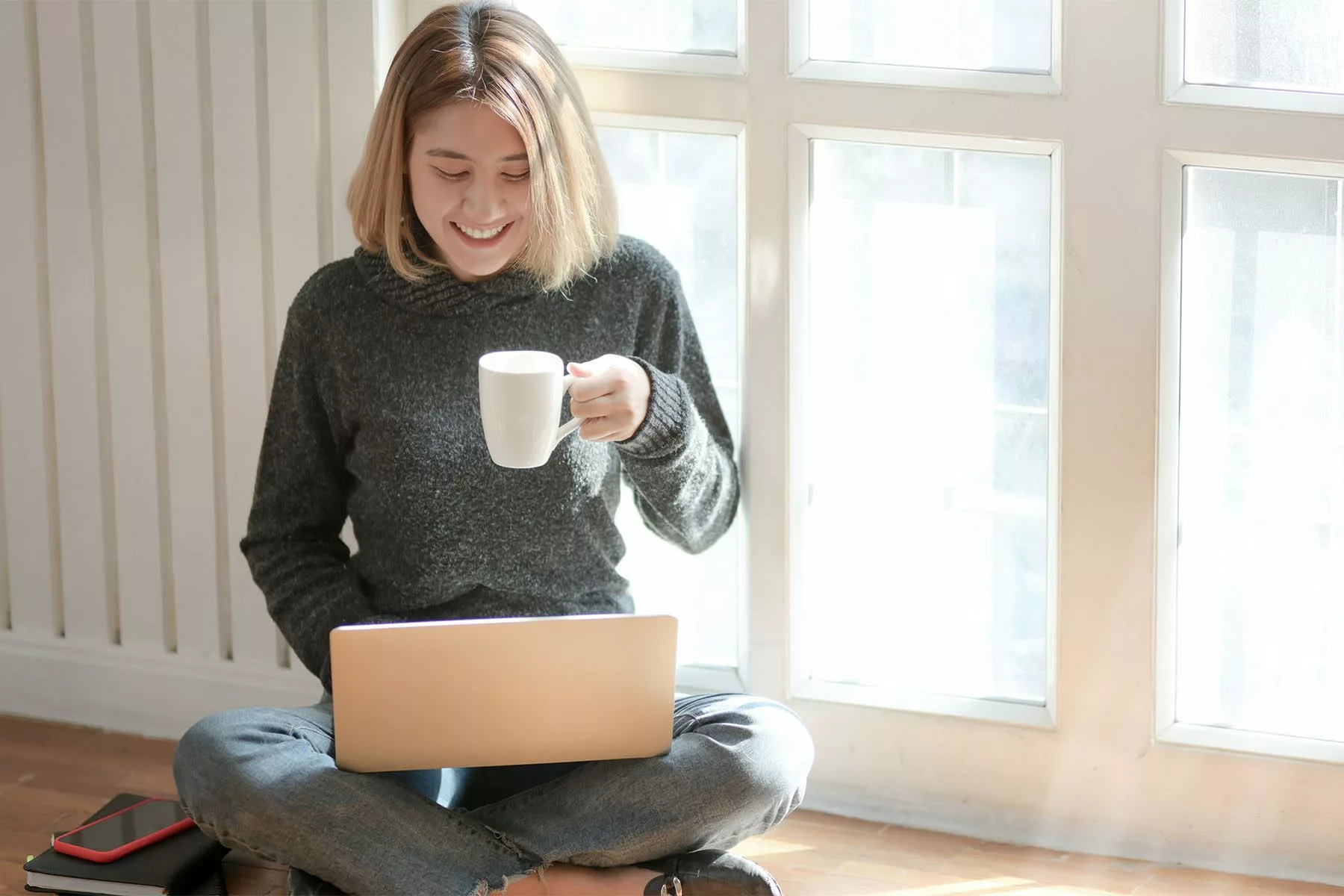 image of smiling person sitting on floor holding a cup of coffee holding a laptop in lap | multifamily qualified lead