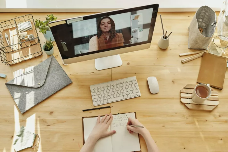 someone writing in a note book in front of a laptop with a woman on video chat