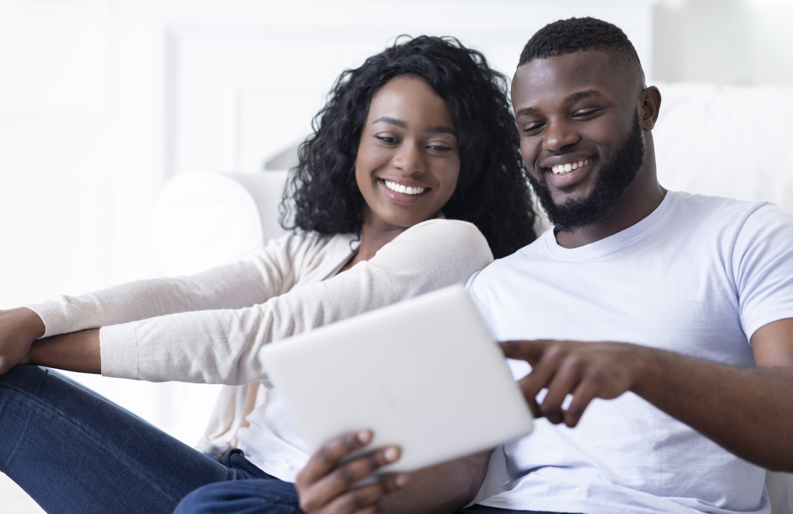 A couple sits on the floor in front of a couch browsing on a tablet for the best property management software for their multifamily community.
