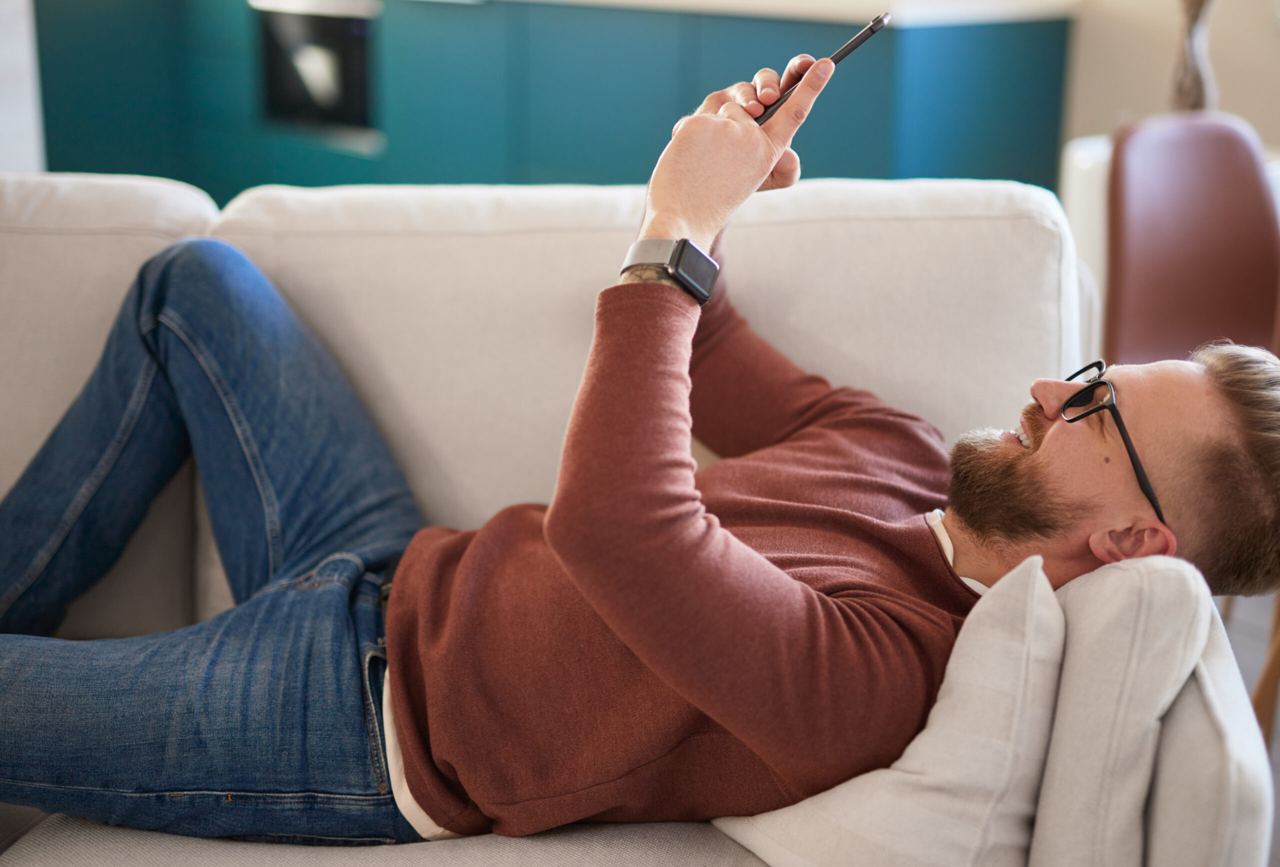 Cheerful person lying on a couch using a smartphone to browse a great multifamily website design