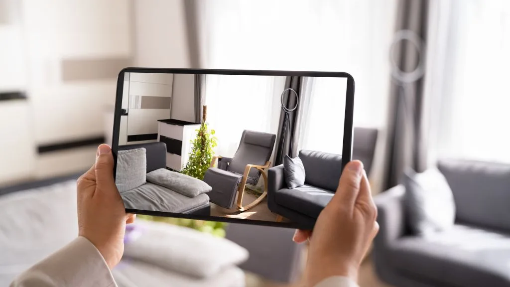 Multifamily Marketing Strategies | PERQ AI Leasing Assistant Person holding a tablet showing an augmented reality view of a modern living room, highlighting interior features like a sofa, armchair, and decor in a multifamily apartment setting.