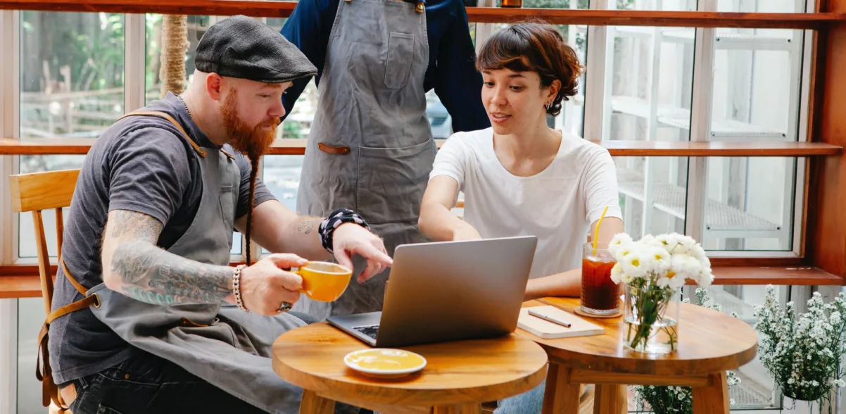 three people at an outdoor cafe gathered around a laptop