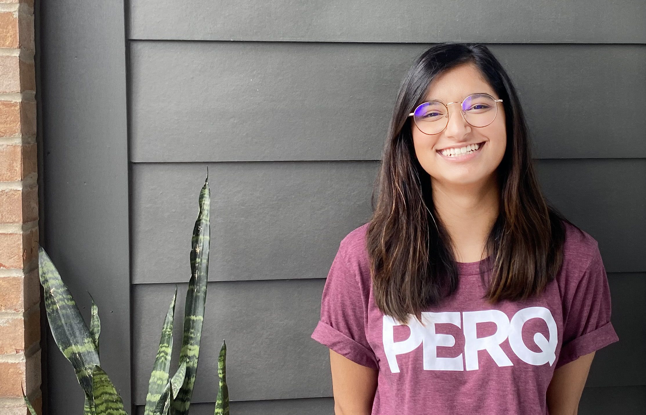 smiling picture of Ibby next to plant and against black wall | PERQ company