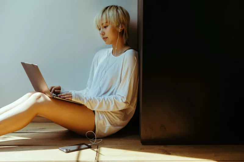 person sitting in a corner working on their laptop and listening to music via earbuds