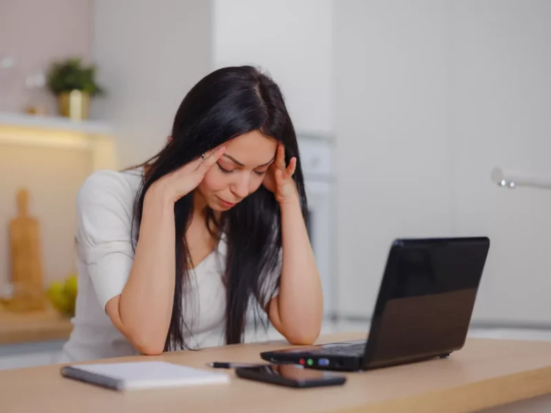 A young woman sits at a desk behind a laptop looking stressed and burnt out from multifamily workforce pains