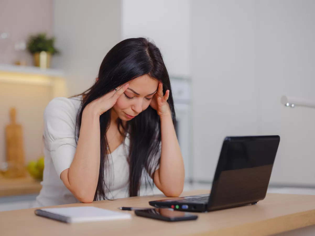 A young woman sits at a desk behind a laptop looking stressed and burnt out from multifamily workforce pains