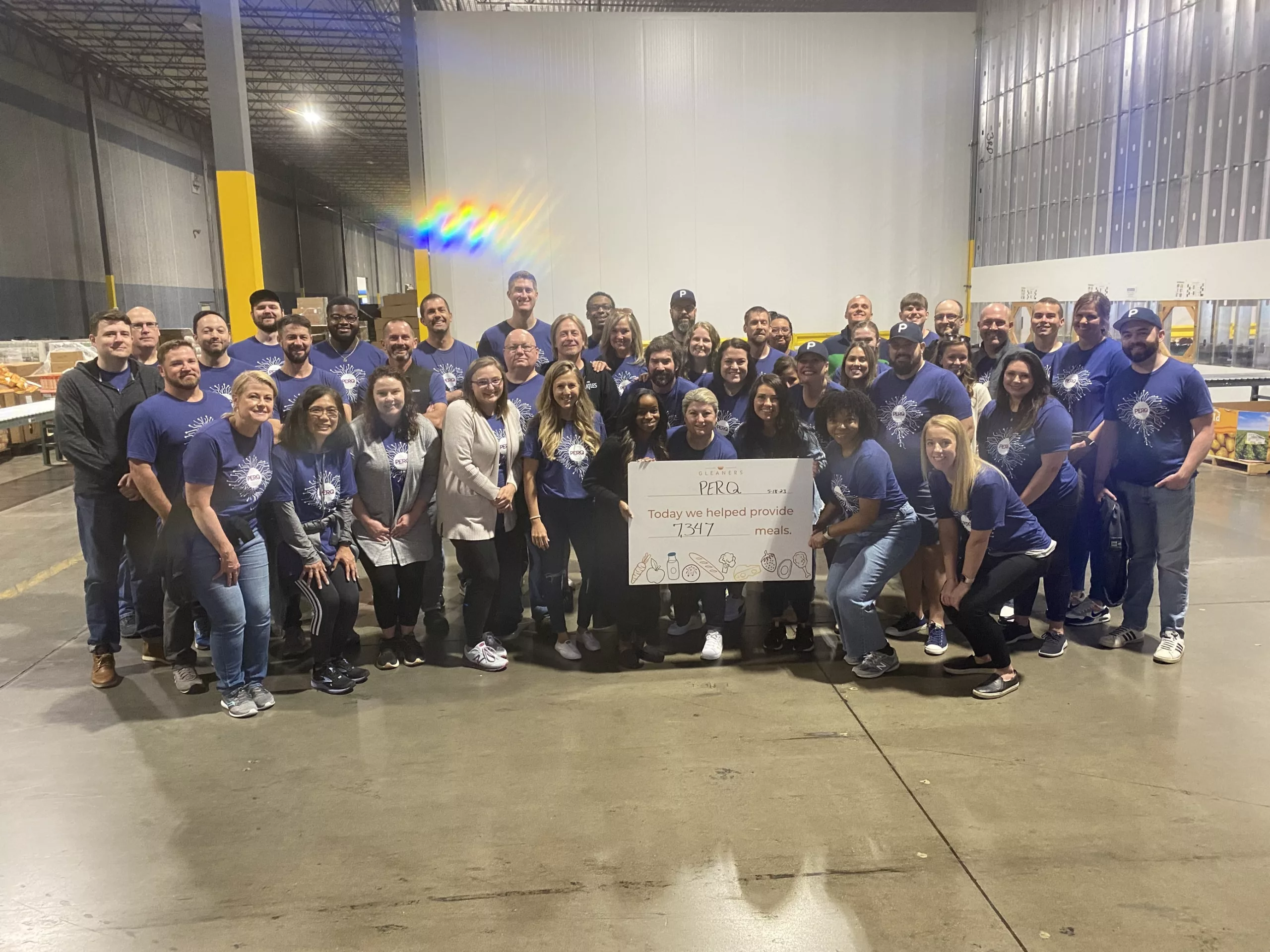 A group picture of the entire PERQ multifamily team volunteering at Gleaner's Food bank holding up a sign showing they provided 7,347 meals.