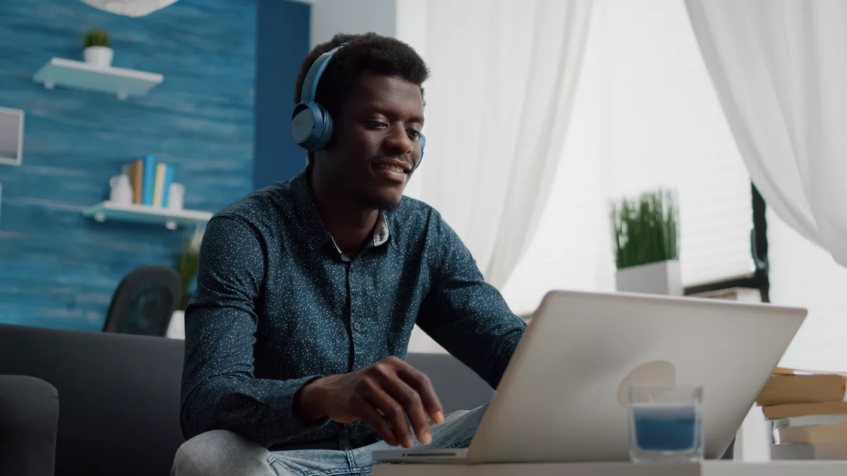 young man sits on a couch with headphones on in front of a laptop on a table while enjoying multifamily digital inbound marketing experiences