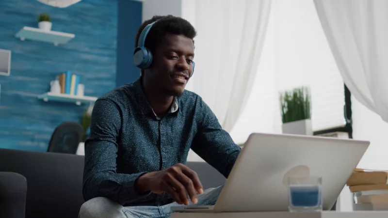 Smiling young man with headphones on looking at open laptop computer