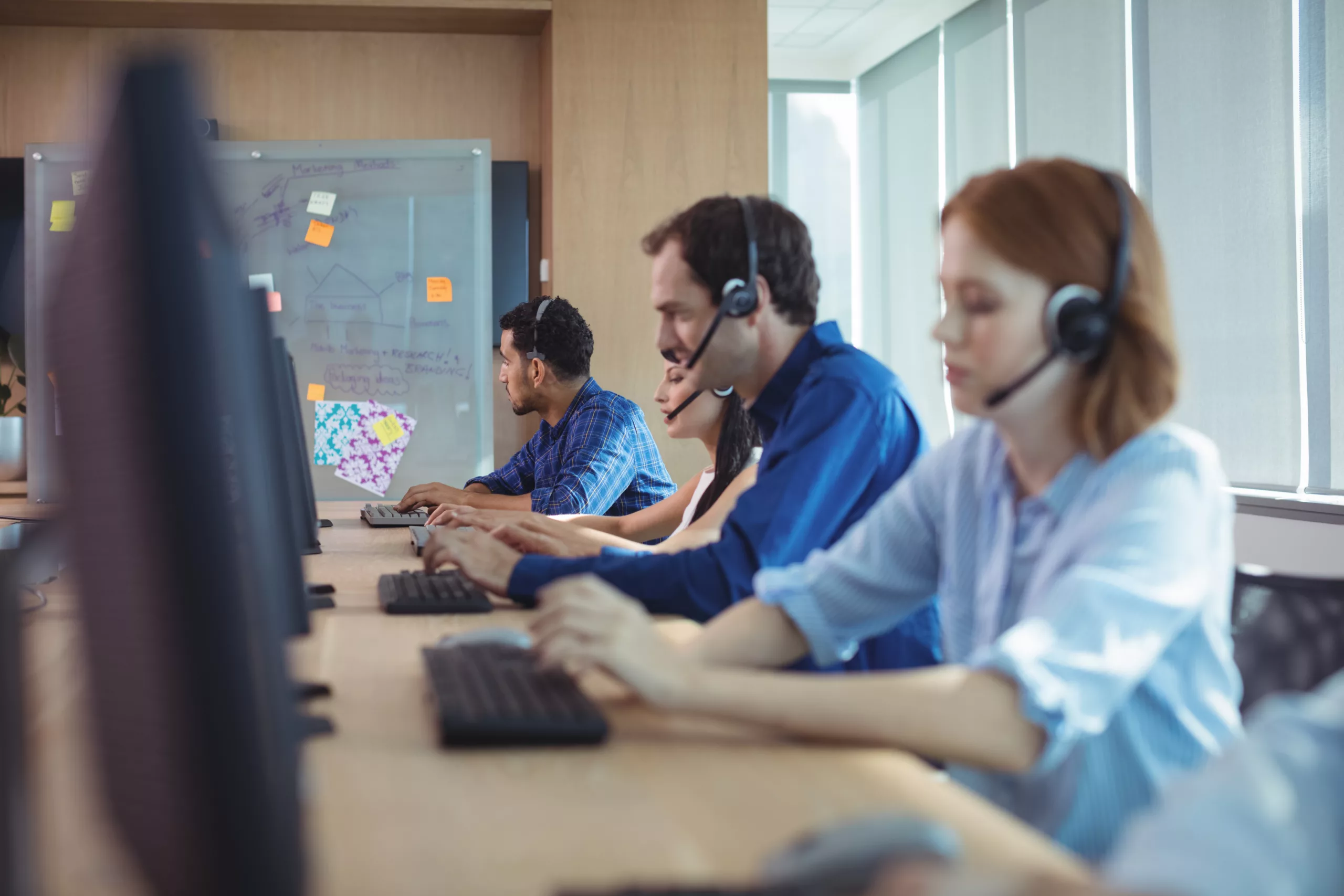 several people sitting behind individual desks with headsets on working in a call center