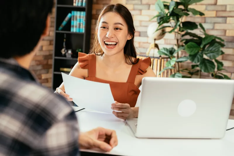 young person holds a piece of paper while sitting at desk talking to another person to connect and explore best practices for marketing to renters