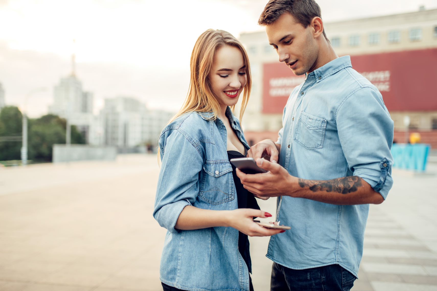 A man and woman smiling while looking at a phone screen.