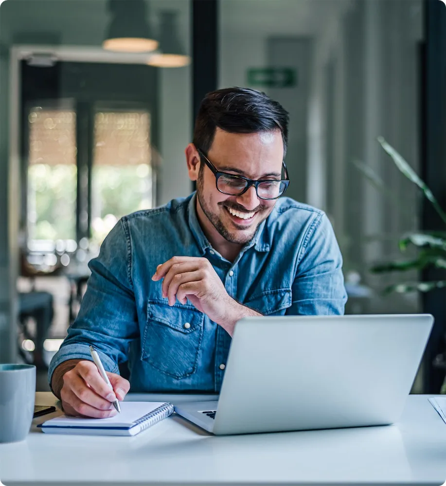 Lead Conversion Solution | PERQ AI Leasing Assistant A guy in a blue shirt looks at a laptop while smiling and taking notes