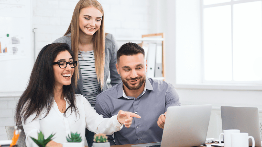 three people gathered excitedly around a laptop