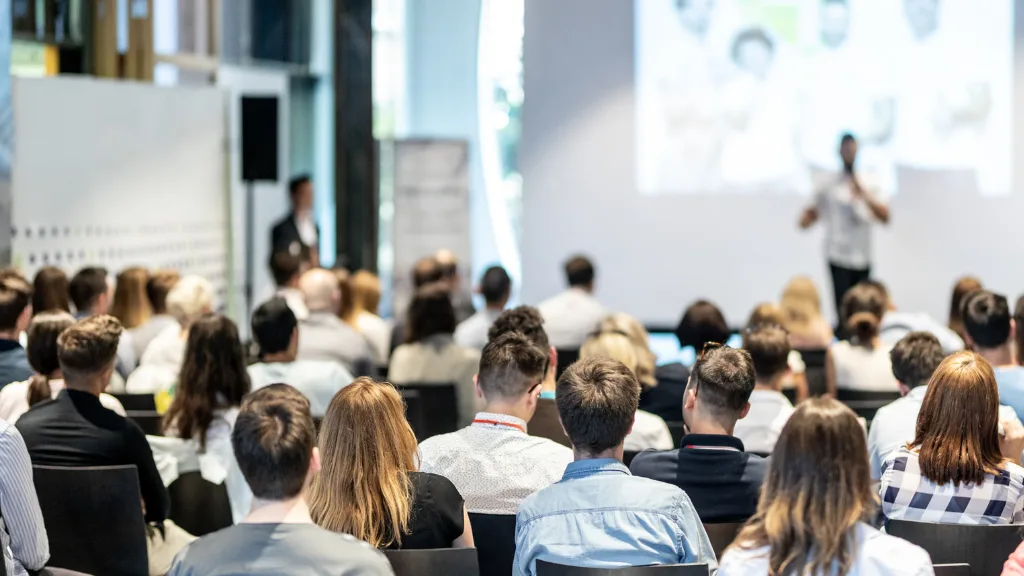 A group of multifamily owners and managers listening to a conference speaker standing on a stage